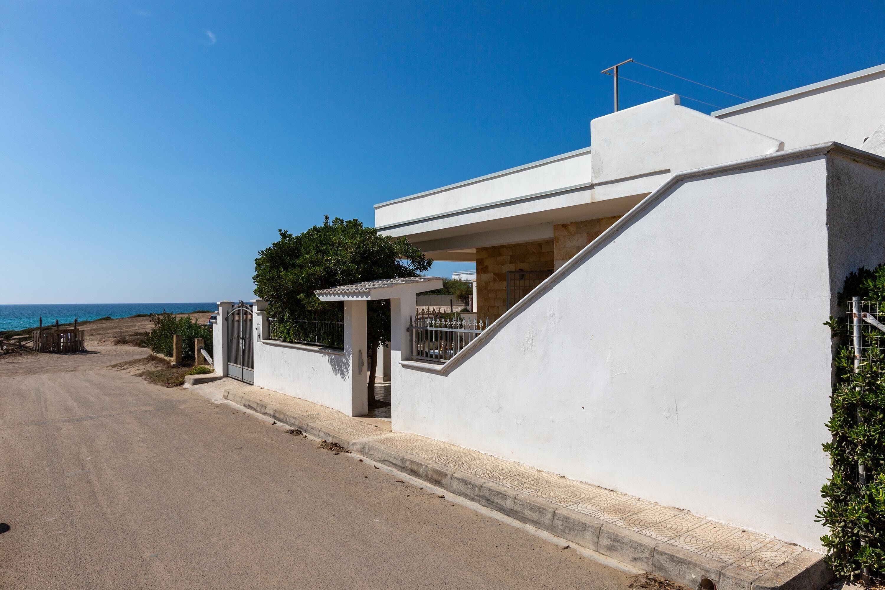 A modern white building with a paved driveway and a gated entrance.