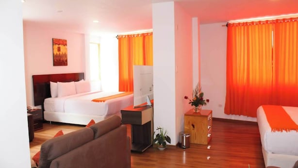 A hotel room with a bed, a sofa, a desk with a computer, and a small plant. - Suites Machupicchu (Machu Picchu)