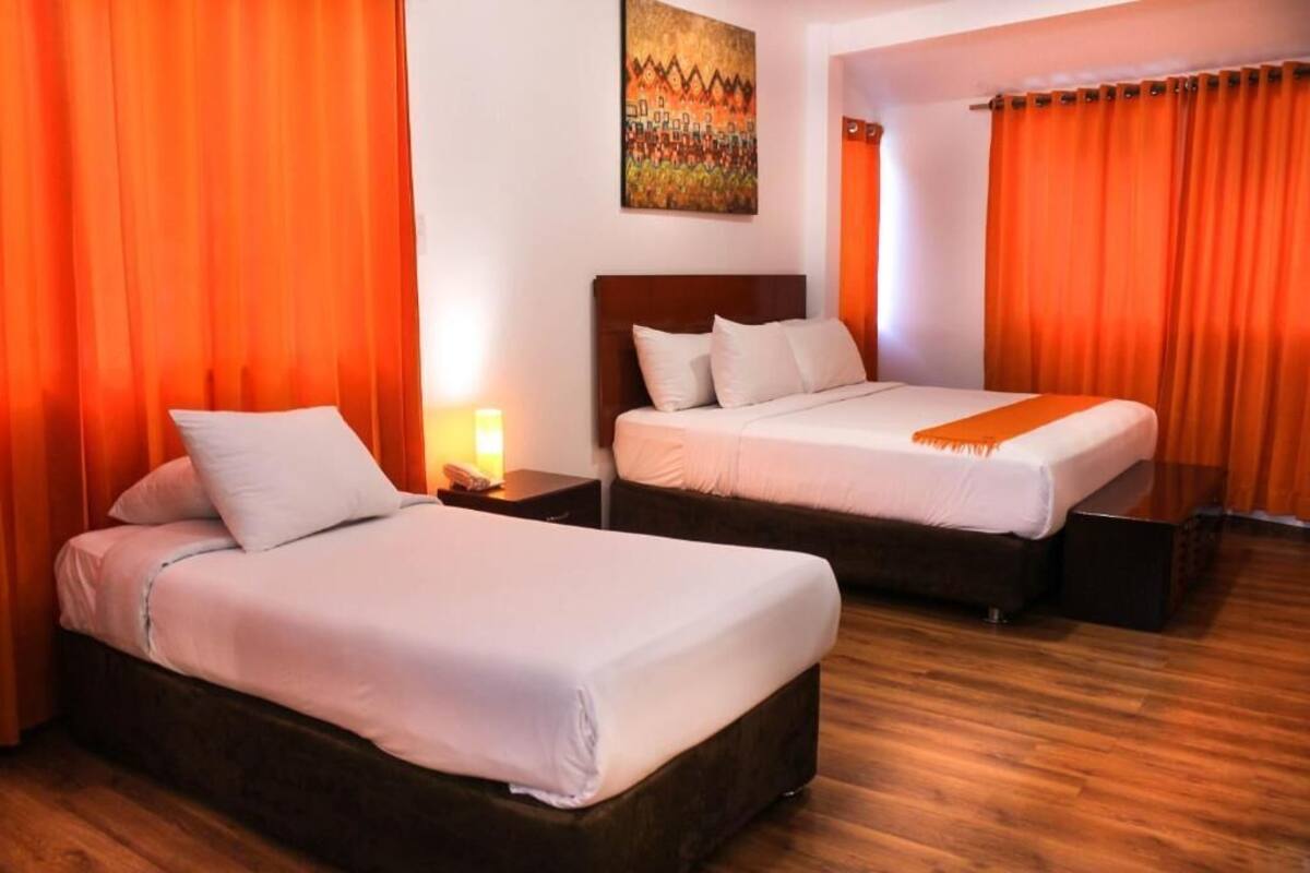 Quarto de hotel com duas camas, piso de madeira e cortinas laranja.