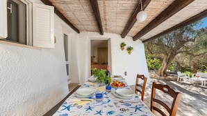 Un área de comedor al aire libre con una mesa preparada para dos personas, rodeada de sillas de madera, bajo un techo de vigas de madera.