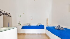 Un dormitorio moderno y minimalista con dos camas, un escritorio de cristal y una pequeña planta en maceta.