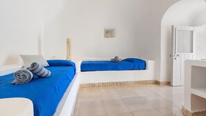Una habitación con dos camas, cada una con ropa de cama azul, una mesita pequeña y un armario blanco.