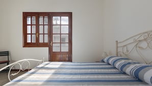 A bedroom with a bed, a wooden door, a metal headboard, and a chair.