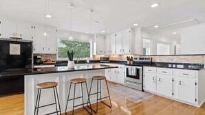 Una cocina moderna con armarios blancos, un refrigerador negro, una isla grande con taburetes e iluminación colgante.