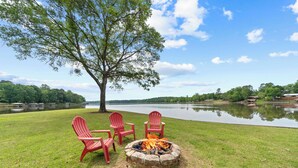Zona de estar al aire libre frente al lago, con una fogata y sillas Adirondack.