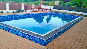 Una piscina rectangular con mosaicos azules y una cubierta de madera alrededor.
