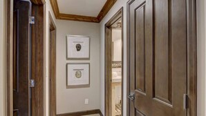 A hallway with wooden doors, framed artwork on the wall, and a tiled floor.