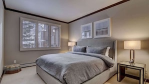 A bedroom with a large bed, two bedside lamps, and a window with blinds.