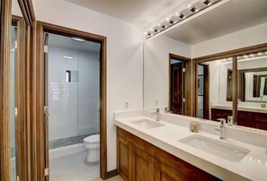 Une salle de bain dotée d’un grand miroir, de deux lavabos et d’un espace douche.