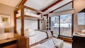 Une chambre avec un lit superposé, une échelle en bois, un bureau et une fenêtre donnant sur un paysage enneigé.