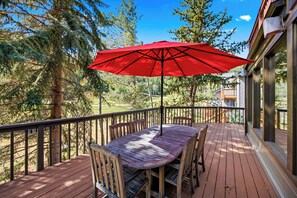 A wooden deck with a table and chairs, an umbrella, and a view of a golf course.