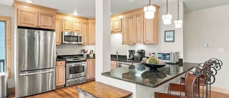 A modern kitchen with stainless steel appliances, wooden cabinets, and a central island with bar stools.