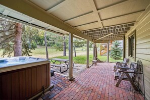 Une terrasse couverte avec un jacuzzi, une table de pique-nique et un coin salon donnant sur une cour verdoyante.