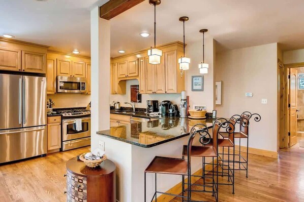A modern kitchen with stainless steel appliances, wooden cabinets, and a central island with bar stools. - Large Family Ski Vacation Home minute from Vail&BC (Avon)