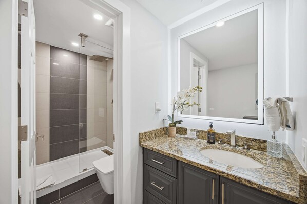 A modern bathroom with a glass shower enclosure, a granite countertop sink, and dark cabinetry. - Renovated Condo with Gondola Access & Walk to Town (Avon)