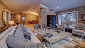 A spacious living room with a large sofa, armchairs, and a coffee table. There is a dining area in the background with a chandelier.
