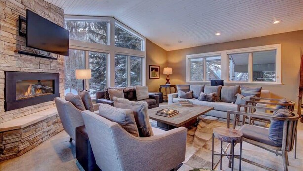 A modern living room with a stone fireplace, large windows, and comfortable seating.