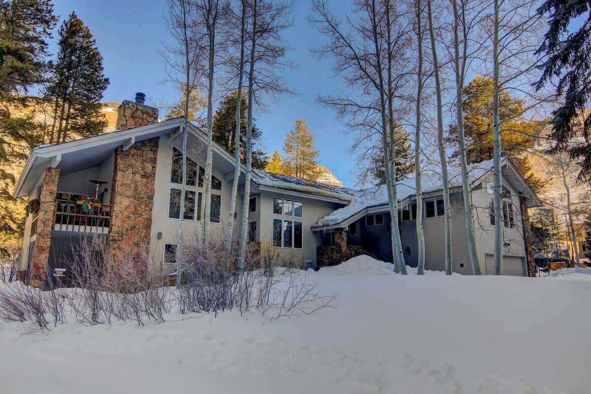 Une maison à deux étages, dotée d’une façade en pierre et de grandes fenêtres, entourée de neige et d’arbres.