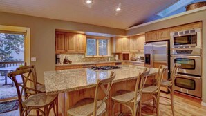 A spacious kitchen with wooden cabinets, a large island with bar stools, stainless steel appliances, and a skylight.