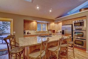 Una cocina amplia con armarios de madera, una isla grande con taburetes de bar, electrodomésticos de acero inoxidable y un tragaluz.