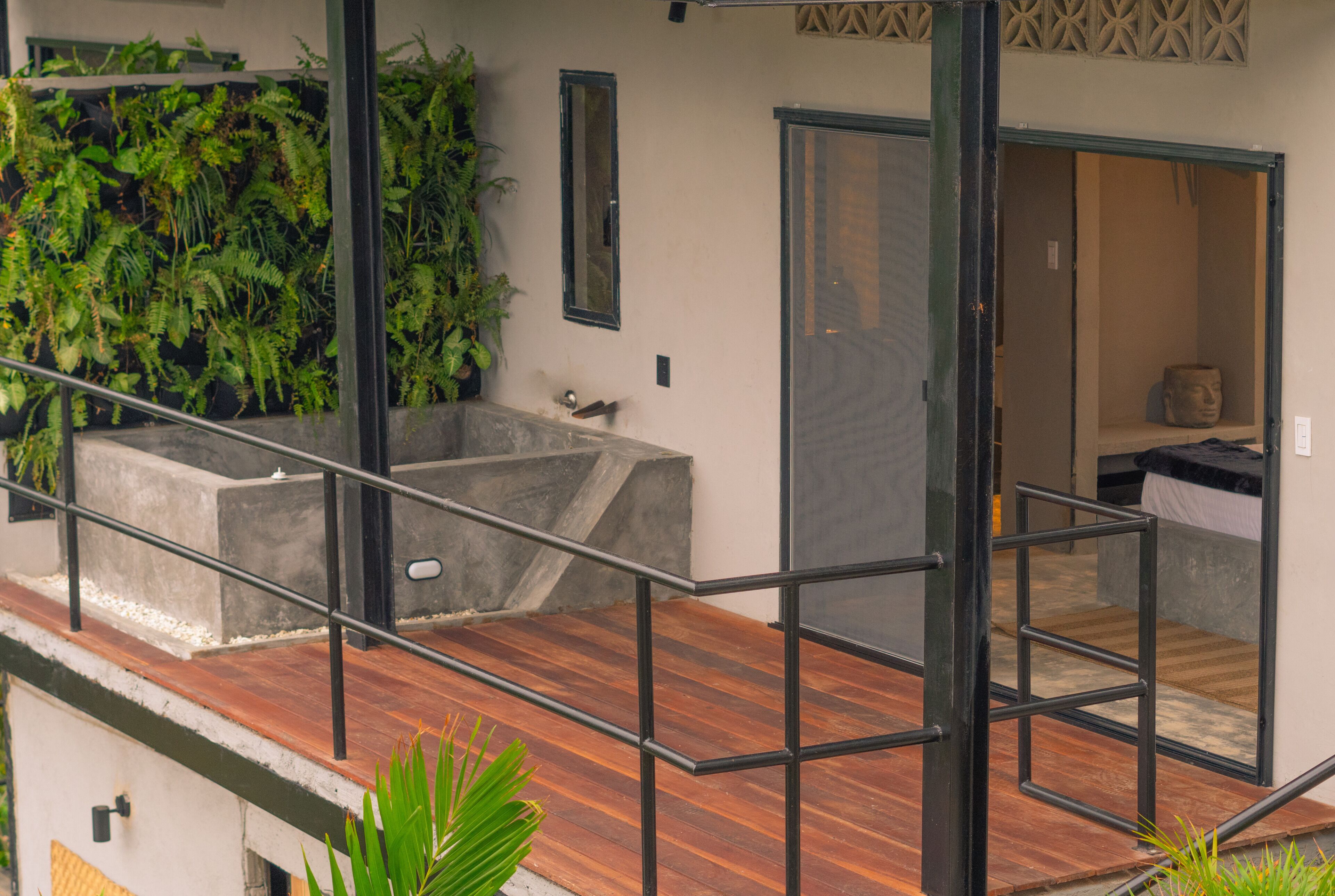 A modern interior with a wooden deck, a concrete planter with greenery, and a visible bathroom with a bathtub.