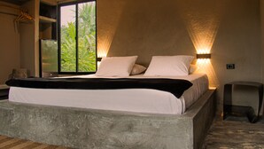Un dormitorio con una cama grande, dos luces fijadas a la pared, un ventanal con vista a zonas verdes y una mesita de noche pequeña.