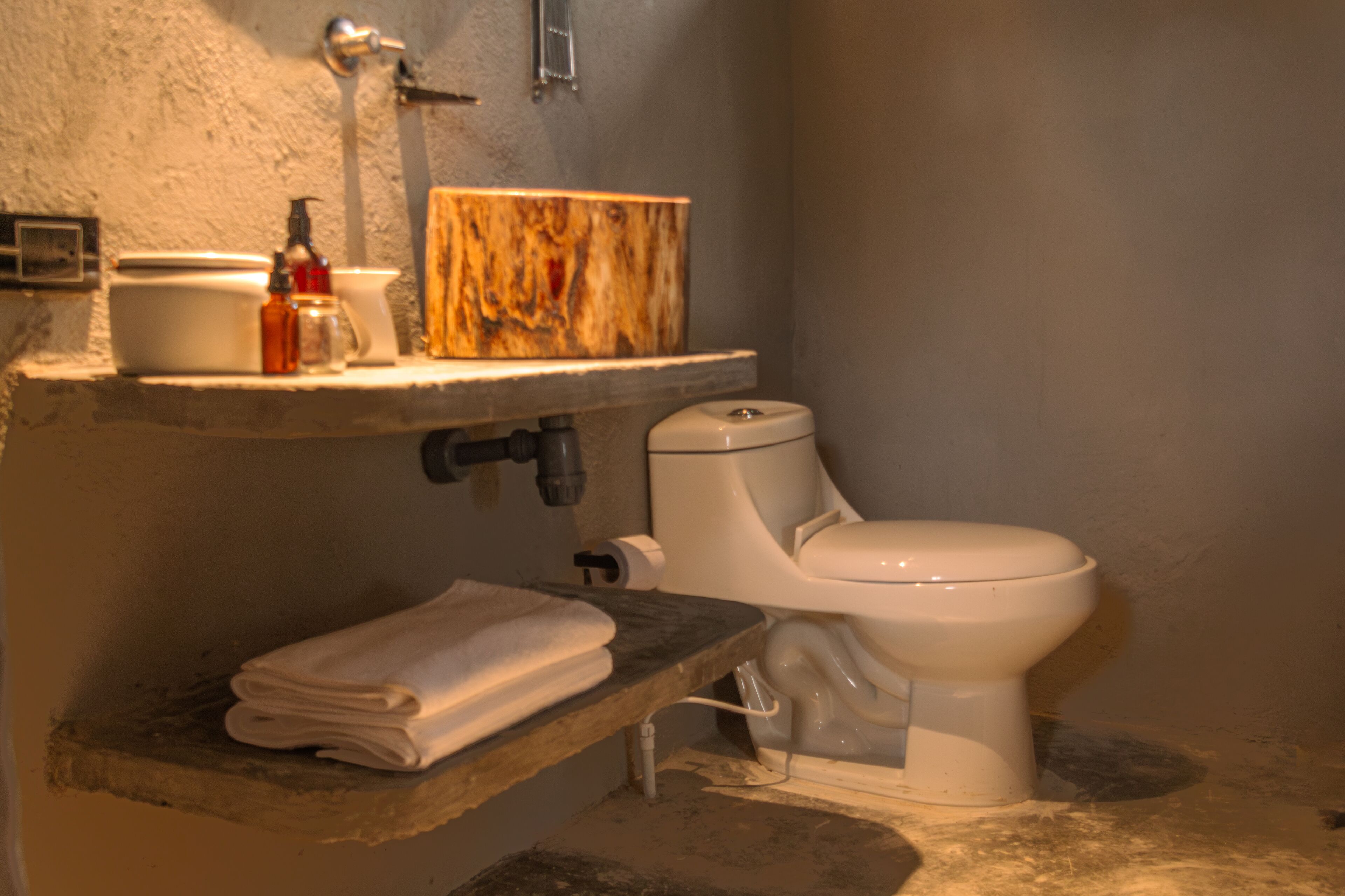 Ein Badezimmer mit Toilette, Waschbecken und einem hölzernen Ablagebrett darüber sowie einem Stapel Handtüchern.