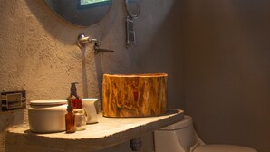 Un baño con un espejo redondo, un inodoro, un lavabo con tocador de madera y una ventana pequeña.