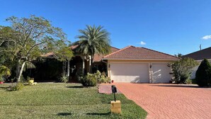 A residential house with a garage, a well-maintained lawn, and a palm tree. - Spacious 4BD/4BA Dream Villa w/LRG Backyard in PSL (Port St. Lucie)