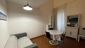 Un espacio habitable pequeño con un sofá, una mesa de comedor con sillas, un televisor y un microondas.