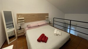 Un dormitorio con cama, mesita de noche, espejo, ventana y barandilla de balcón.