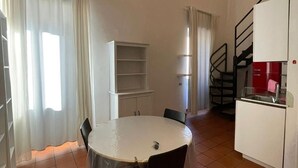 Una cocina compacta con una mesa redonda, sillas, un refrigerador blanco y una escalera.