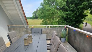 Une terrasse extérieure avec une table et des chaises, un pot de fleurs et une vue sur un cycliste sur une piste.