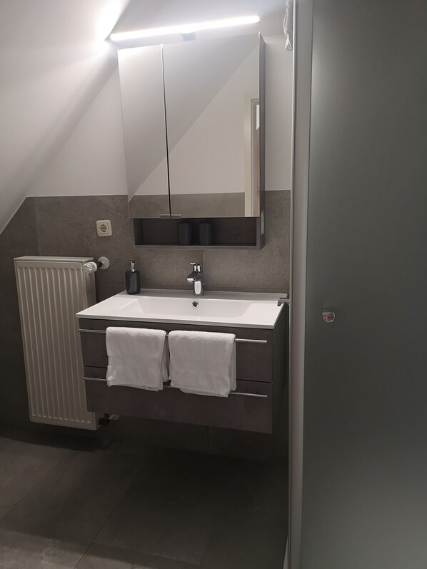 A modern bathroom with a white sink, two towel racks, a mirror, and a radiator.