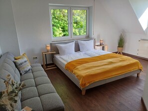 A bedroom with a bed, a sofa, a window, and a plant.