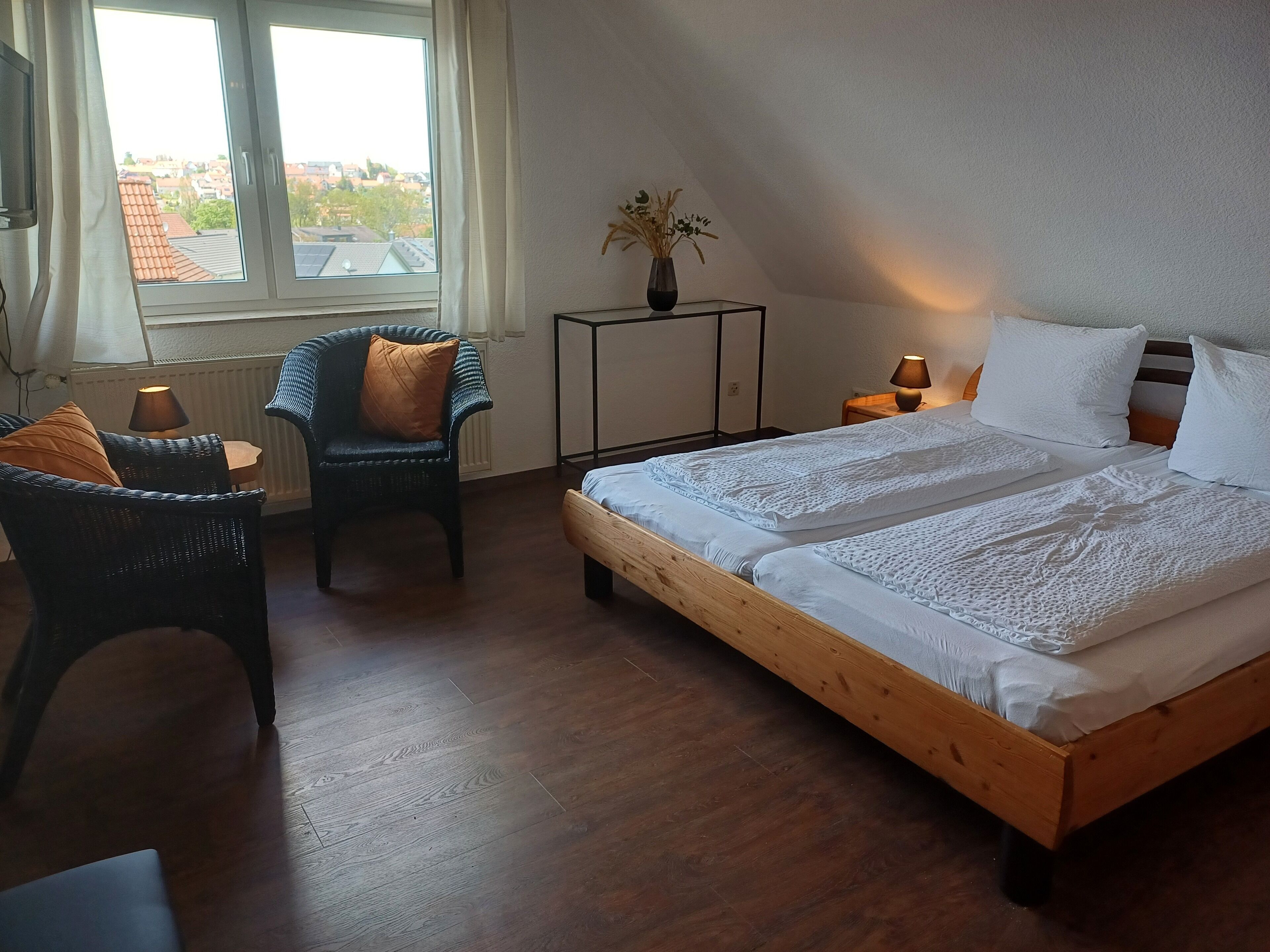 Une chambre avec un grand lit, deux chaises, une petite table, une lampe et une vue sur la ville par la fenêtre.