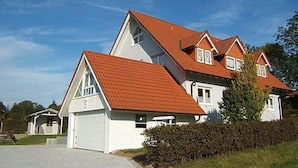 Une maison à deux étages avec un toit recouvert de tuiles rouges, un garage et une pelouse bien entretenue.