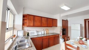 Une cuisine avec des meubles en bois, un four à micro-ondes, un grille-pain, un évier et un coin repas avec une table mise pour deux personnes.