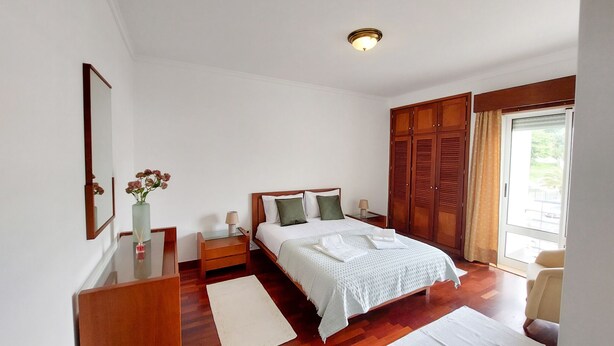 Une chambre à coucher avec un lit en bois, une table de chevet, une commode, un miroir et une fenêtre avec des rideaux.