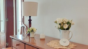 Une commode en bois avec des tiroirs, un vase avec des fleurs, une lampe et un miroir.