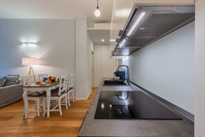 A modern kitchen with a built-in stove, a sink, and a compact dining area with a table and chairs. - Sweett | San Senatore (Milano)