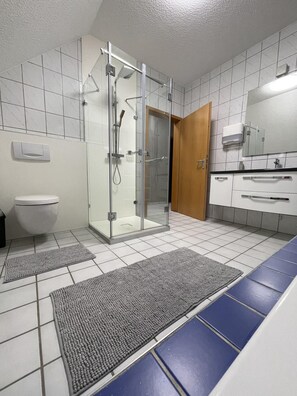 Uma casa de banho moderna com cabine de duche em vidro, sanita, lavatório com espelho e porta de madeira.