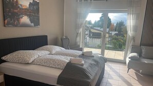 Une chambre à coucher avec un lit, une chaise, une vue sur l’extérieur et un tableau au mur.