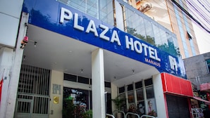 Das Plaza Hotel mit auffälligem blauen Schild, einem bewachten Eingangsbereich und Pflanzgefäßen nahe dem Eingang.