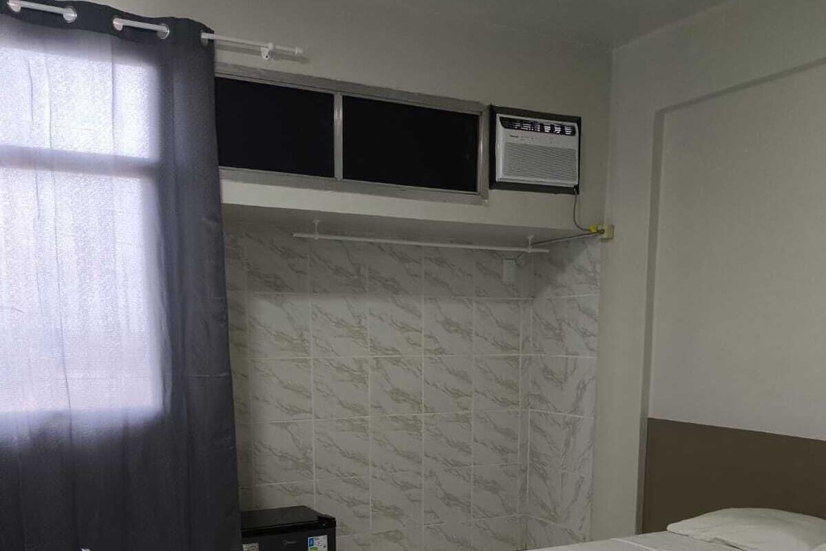 Ein Hotelzimmer mit einem Einzelbett, einem Schreibtisch, einem Stuhl, einem Heizgerät und einem fenster mit Vorhängen.