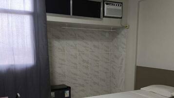 Ein Hotelzimmer mit einem Einzelbett, einem Schreibtisch, einem Stuhl, einem Heizgerät und einem fenster mit Vorhängen.