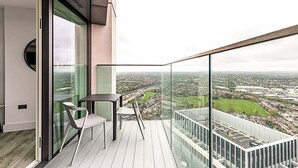 A modern balcony with a glass railing, a table, and two chairs, overlooking a cityscape. - Modern Sky-High Flat In North Acton (London)