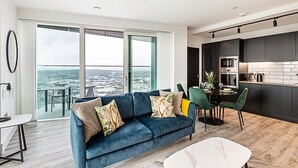 A modern living room with a blue sofa, dining area, and kitchen. - Modern Sky-High Flat In North Acton (London)