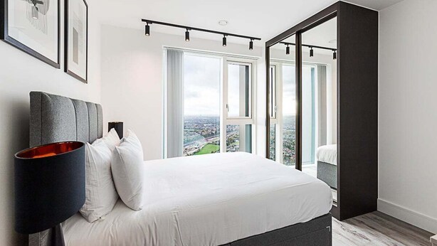 A modern bedroom with a large bed, a view of the city, and a sliding door to a balcony. - Modern Sky-High Flat In North Acton (London)