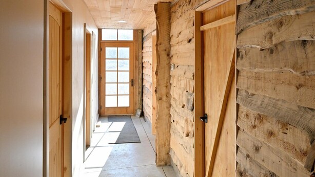 A hallway with wooden walls and doors, leading to a bright room with a large window. - Renovated Rustic Lodge/Historic property.
Hike, fish, star gaze. w/artist studio (Port Washington)